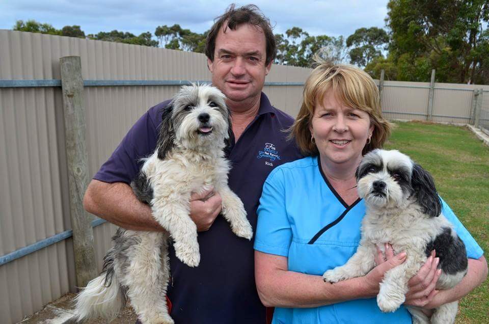 Rick and Ann standing by the exercise yard fence, each holding one of the dogs staying with them